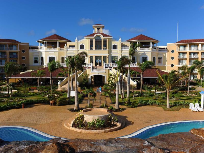 Resort di lusso con piscina, paesaggio verde e edificio principale su più piani sotto un cielo limpido.