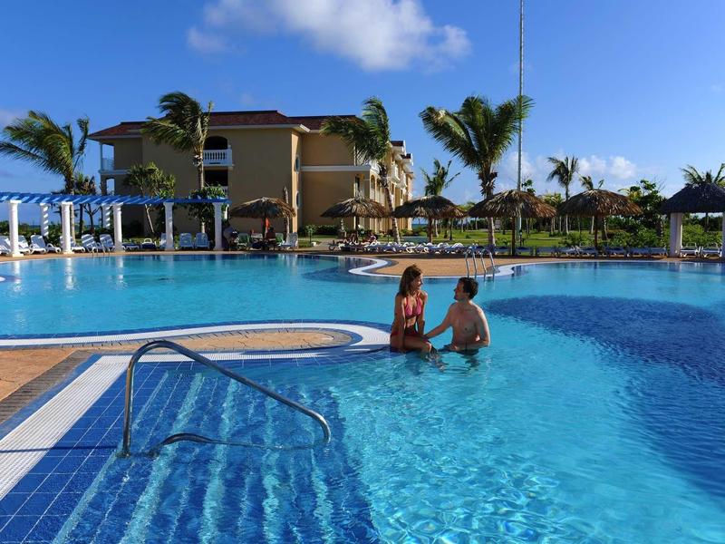 Due persone in una piscina di un hotel tropicale con palme e cielo azzurro