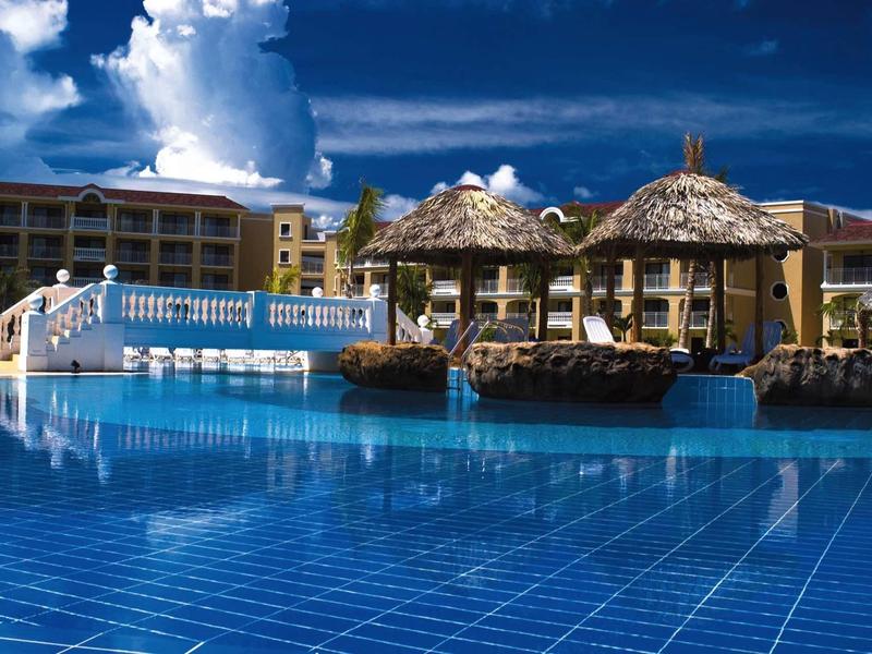 Grande piscina con pavimento piastrellato blu e lettini di paglia in un resort.