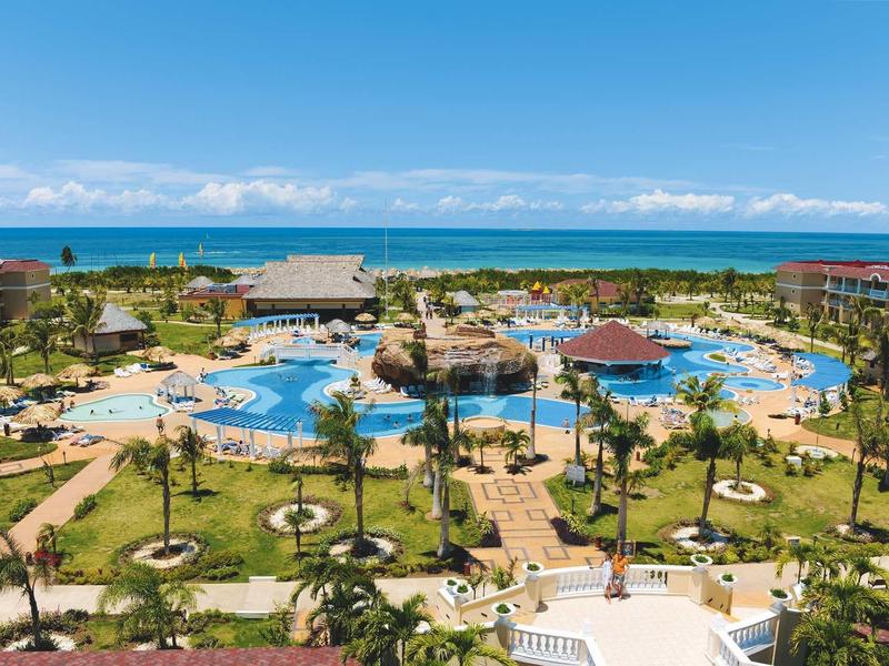Ampio resort con piscina, palme e vista mare sotto cielo limpido.