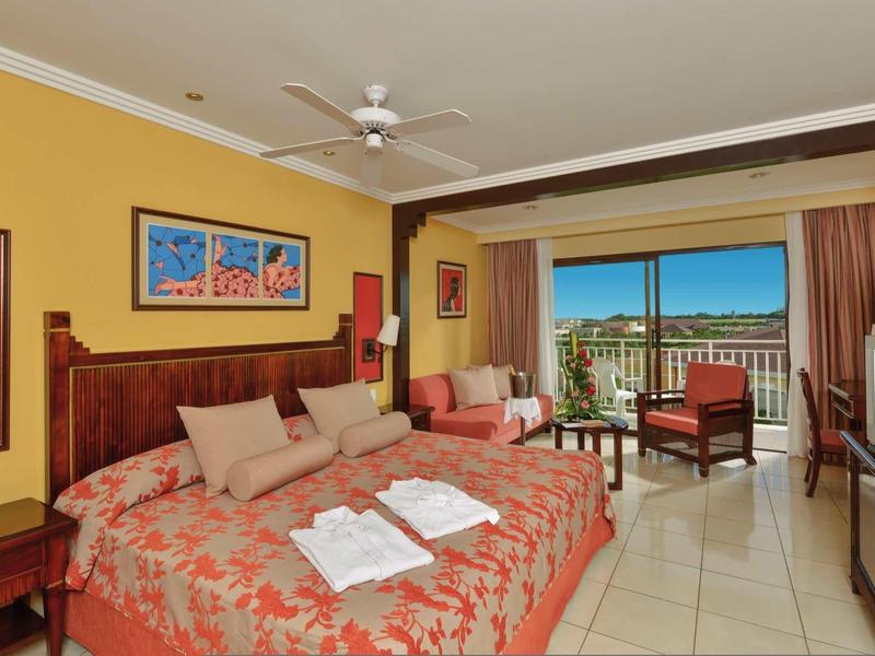 Camera d'hotel con letto matrimoniale, zona salotto e balcone con vista sulla città di giorno.