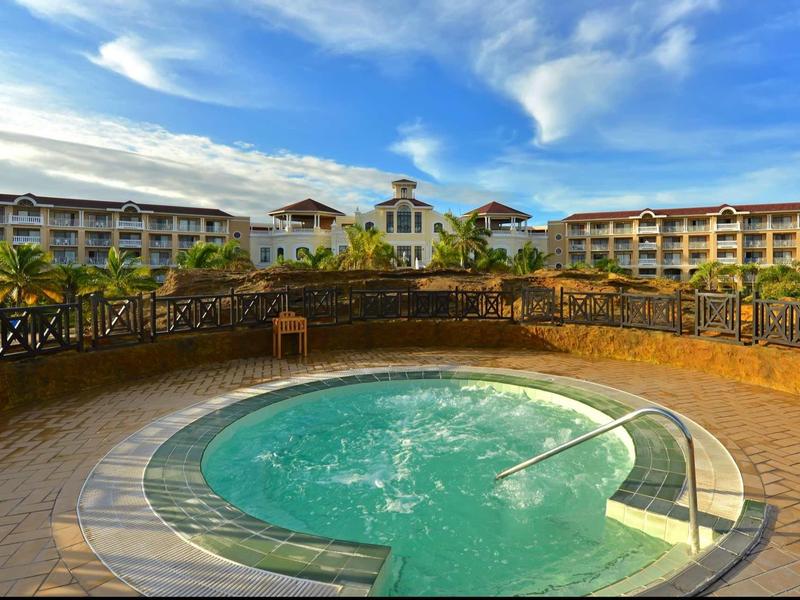 Vasca idromassaggio rotonda con getti d'acqua su una terrazza davanti a un hotel con palme.