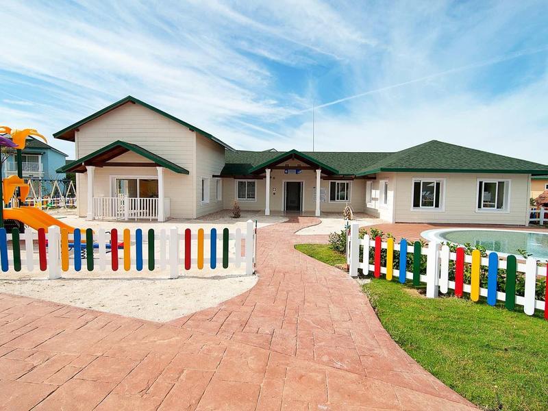 Lichtgekleurd eengezinswoning met kleurrijk houten hek en speeltuin in de tuin.