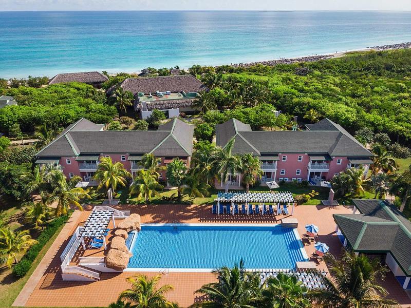 Uitzicht op hotel met groot zwembad, ligstoelen en oceaan op de achtergrond.