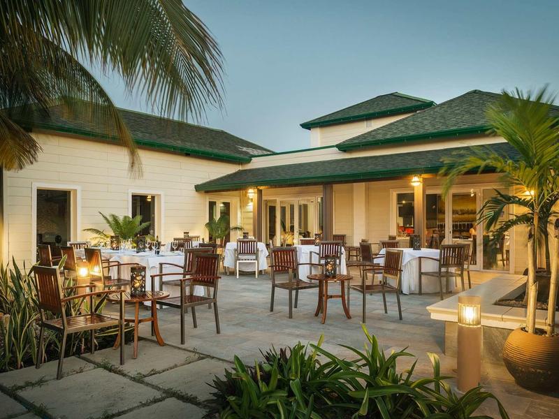 Verlichte hotelterras met gedekte tafels en tropische planten bij schemering.