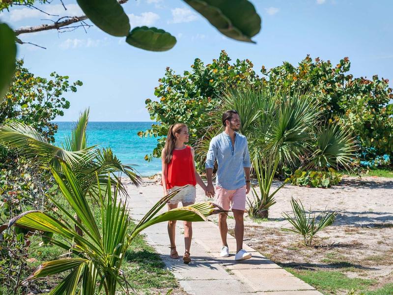 Stel wandelt over een strandpad omringd door tropische planten met uitzicht op de oceaan.