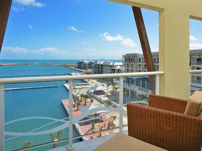 Balkon s proutěným křeslem s výhledem na přístav a moře pod modrou oblohou