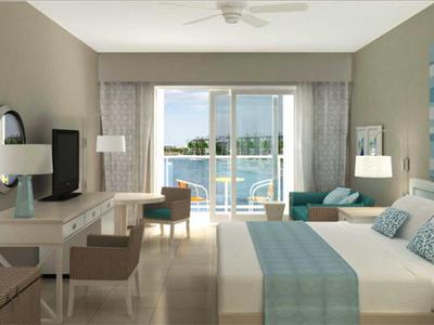 Camera d'hotel moderna con letto grande, scrivania e vista sull'acqua tramite porta scorrevole in vetro.