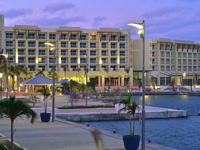 Velká hotelová budova u vody s bazénem a palmami při soumraku.