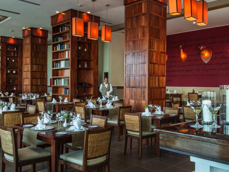 Ristorante elegante con mobili in legno, tovaglie bianche e lampade a sospensione arancioni moderne.