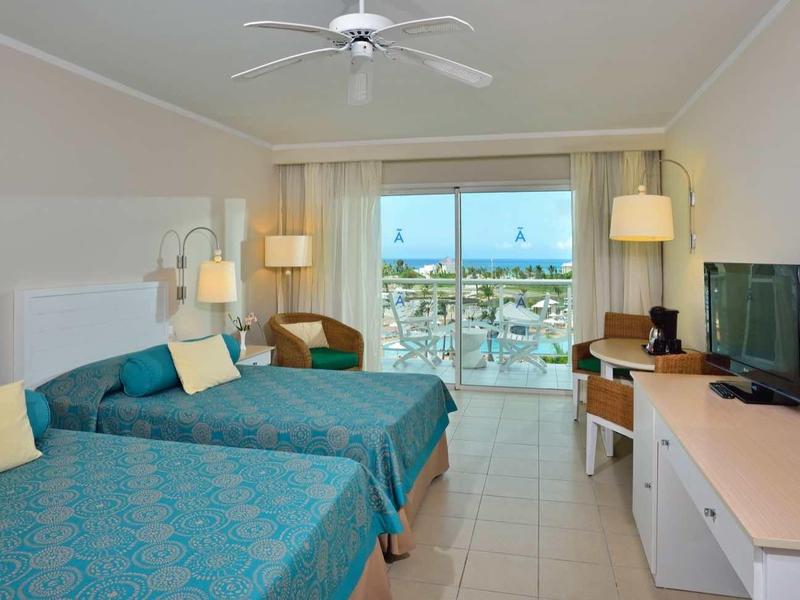 Camera d'hotel luminosa con due letti, zona salotto e vista sul mare.