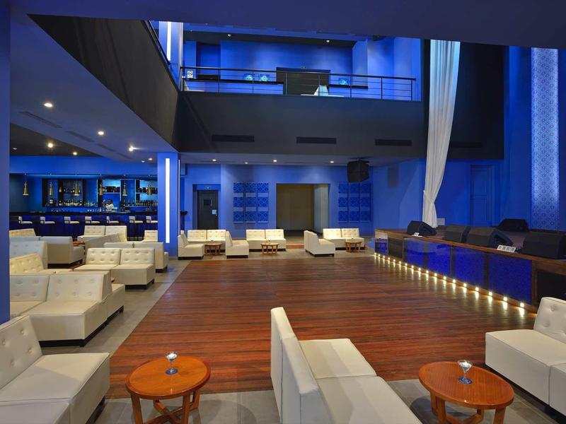 Hall moderno di un hotel con divani bianchi, pavimento in legno e illuminazione blu.