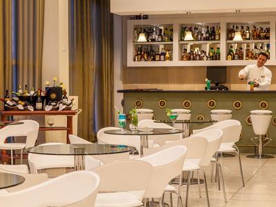 Espace bar d'hôtel moderne avec des chaises blanches, des tables et un barman derrière le bar.