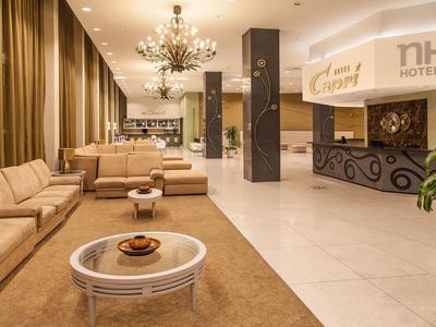 Hall d'hôtel lumineux avec canapés modernes, lustres et comptoir d'accueil.