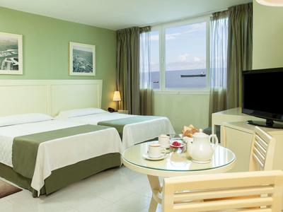 Chambre d'hôtel avec deux lits simples, une table avec service à thé et fenêtre avec vue sur la mer