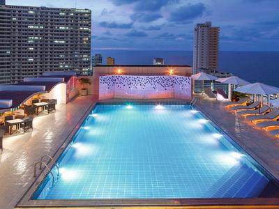 Piscine à débordement éclairée sur terrasse sur le toit avec vue sur la ville et la mer au crépuscule.