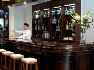 Elegant bar with dark wood, bar stools, and a bartender preparing a drink.