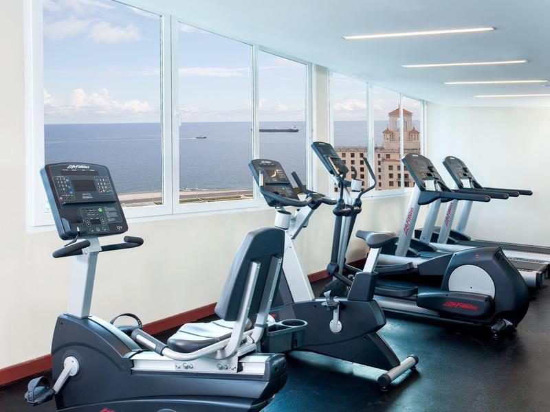 Salle de sport lumineuse avec appareils d'exercice et grandes fenêtres donnant sur la mer.