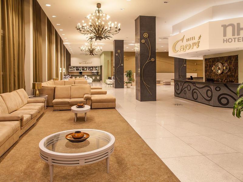 Hall d'hôtel lumineux avec canapés modernes, lustres et comptoir d'accueil.