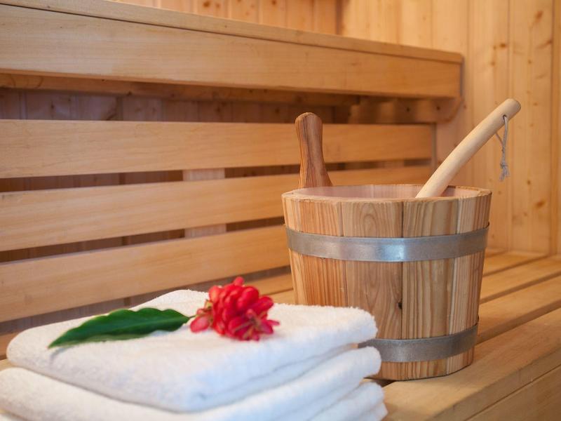 Intérieur de sauna avec bancs en bois, un seau et des serviettes blanches avec une fleur rouge.