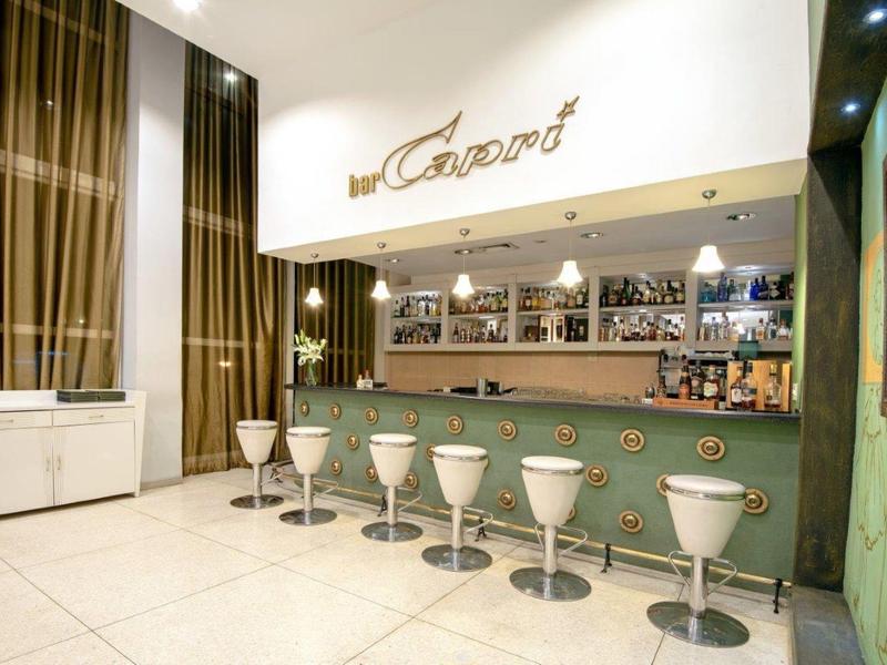 Un bar d'hôtel élégant avec des tabourets blancs et un éclairage moderne.