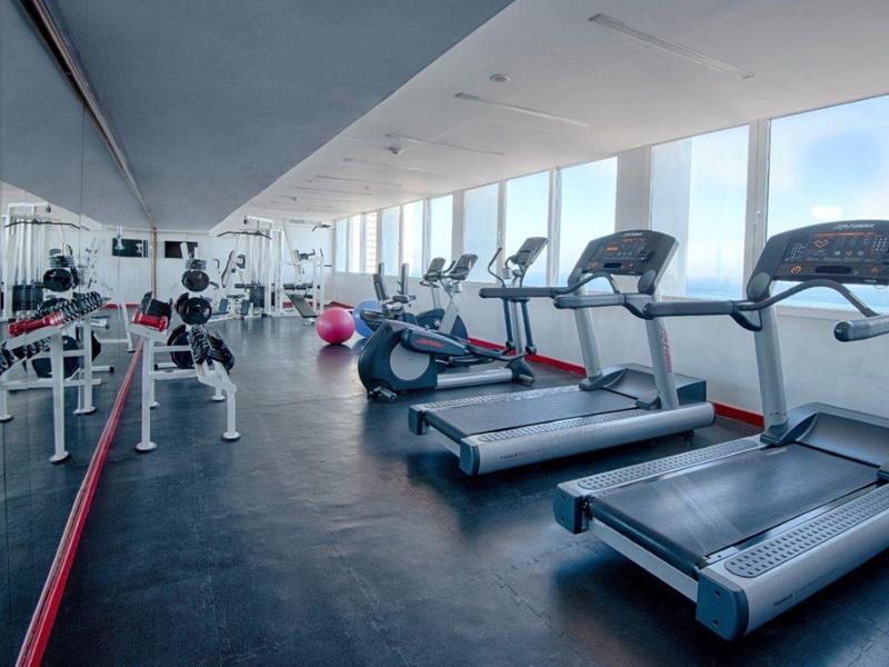 Salle de sport lumineuse avec tapis de course et équipements près de grandes fenêtres avec vue.