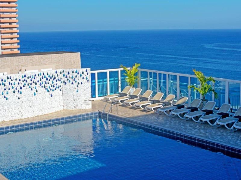 Piscine bleue avec chaises longues et vue sur la mer par une journée ensoleillée.