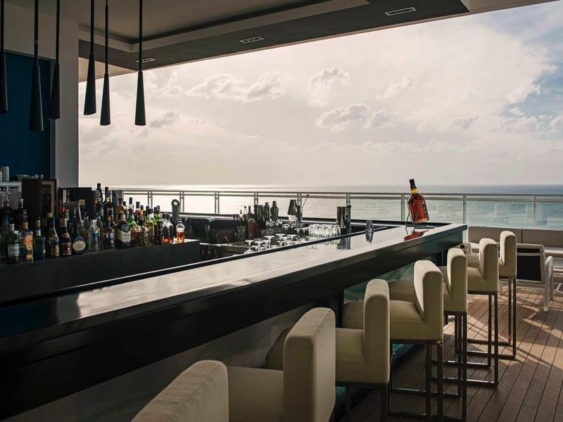 Bar dell'hotel moderna con sgabelli e vista mare al tramonto.
