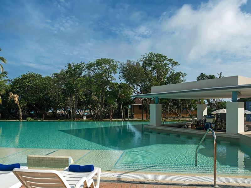 Grande piscina con lettini e alberi sullo sfondo in una giornata di sole.
