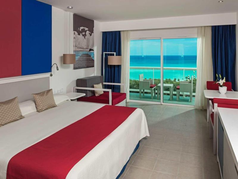 Camera d'hotel moderna con vista mare e balcone, elegantemente decorata in rosso, blu e bianco.