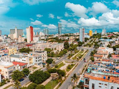Pohled na město s parky, vysokými budovami a širokou silnicí pod modrou oblohou.