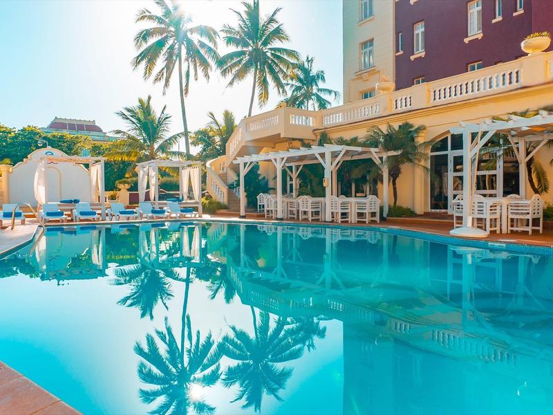 Čistý bazén s lehátky a palmami ve slunečné hotelové zahradě.