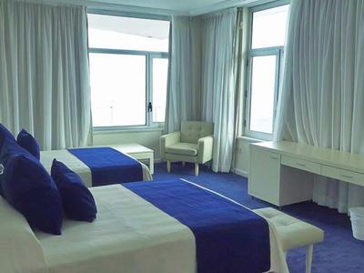 Chambre d'hôtel avec deux lits simples, jetés de lit bleus, grandes fenêtres et télévision.