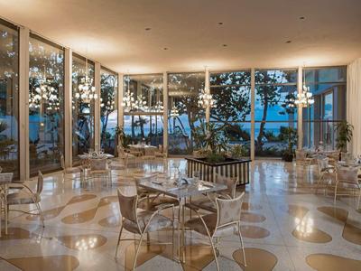 Sala da pranzo moderna con pareti di vetro che offrono vista su alberi esterni e cielo azzurro.
