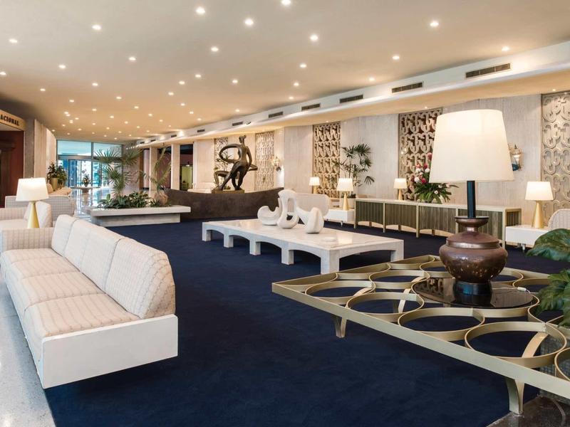 Hall d'hôtel moderne avec canapés blancs, tapis bleus et décorations élégantes.