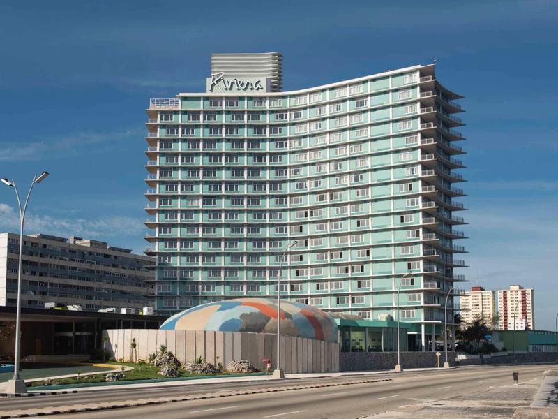 Hôtel moderne incurvé avec de nombreuses fenêtres sous un ciel clair.