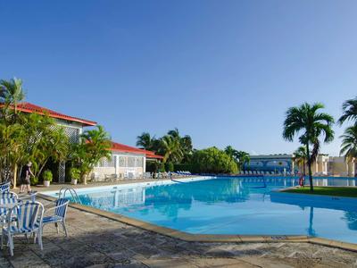 Une zone de piscine calme avec des chaises et des palmiers sous un ciel clair.