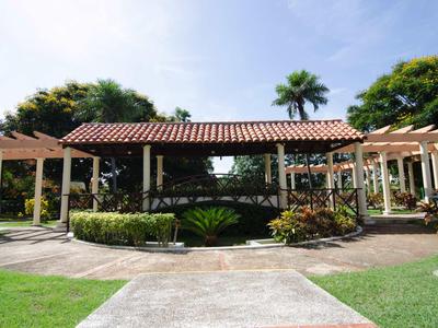 Un jardin avec pelouse bien entretenue, allées, un kiosque et des arbres sous un ciel bleu.