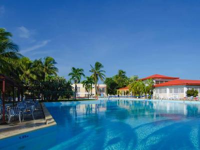 Grande piscine d'hôtel avec chaises longues et palmiers sous un ciel clair