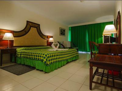 Camera d'albergo con letto a quadri verdi, comodini con lampade e una scrivania.