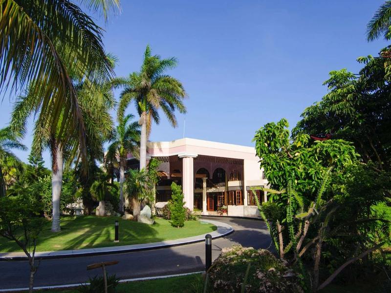 Edificio dell'hotel moderno circondato da palme e verde sotto un cielo azzurro limpido.