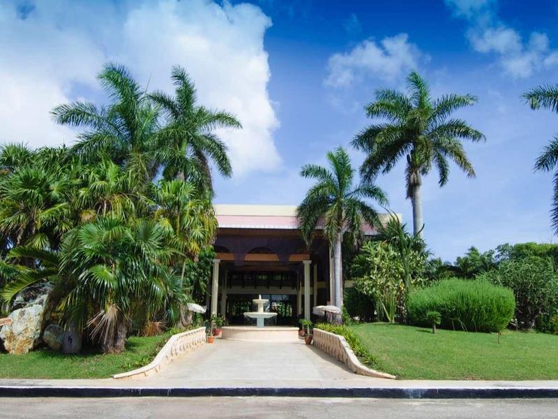 Villa di lusso con palme, prato verde e vialetto ampio sotto un cielo azzurro.