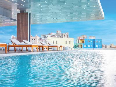 Moderner Pool mit Liegestühlen und Blick auf bunte Gebäude bei sonnigem Himmel.