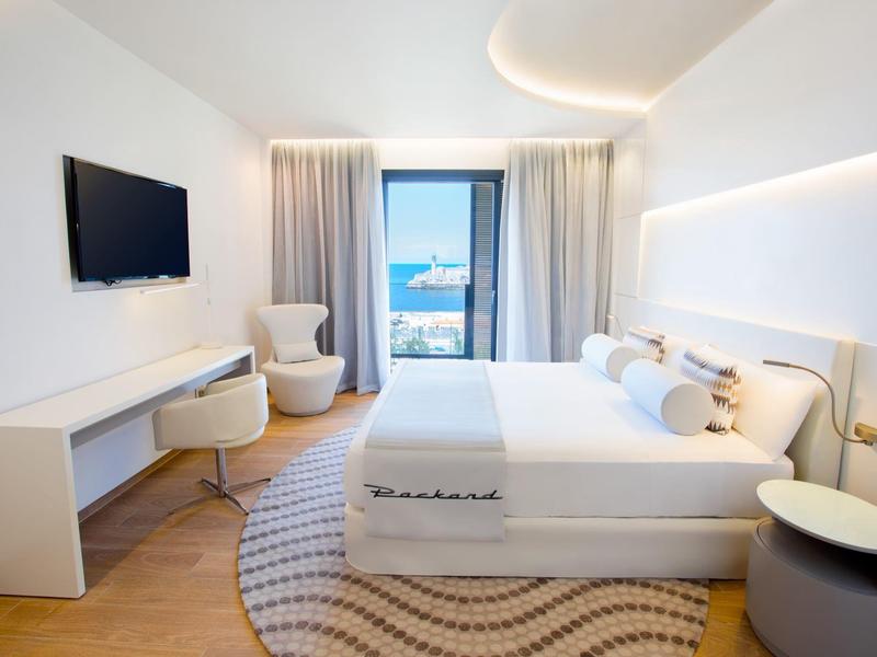 Habitación moderna con cama, escritorio y ventana con vista al mar.