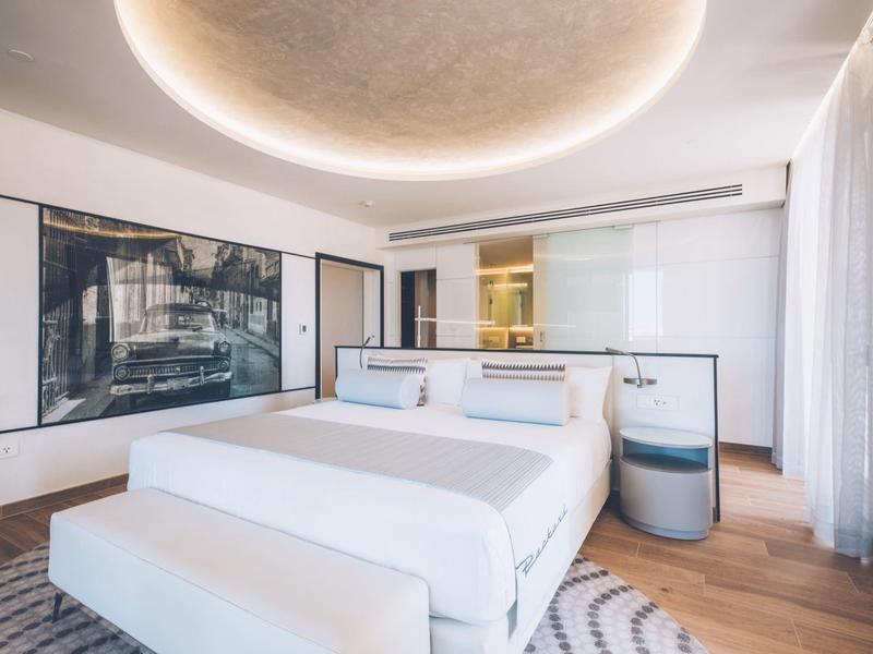 Habitación de hotel luminosa con cama grande, arte moderno y suelo de madera.