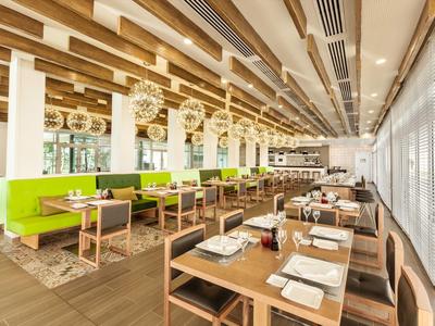 Sala da pranzo luminosa con tavoli in legno e divanetti verdi in un hotel moderno.