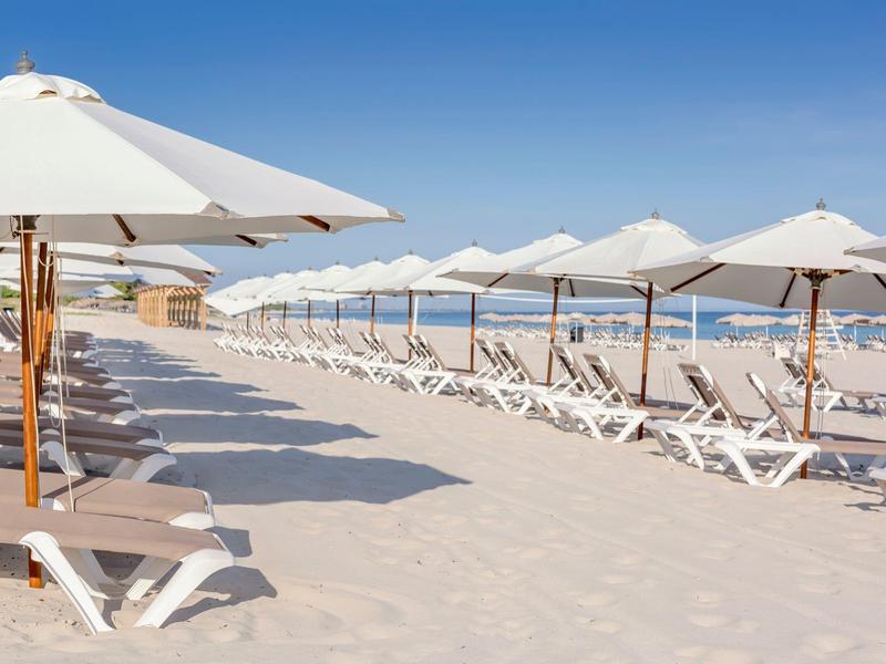 Lettini bianchi con ombrelloni su una spiaggia sabbiosa vicino al mare.