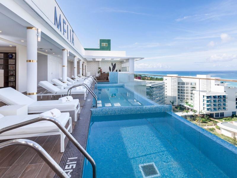 Piscina a sfioro sul tetto con lettini e vista sul mare e sugli edifici.