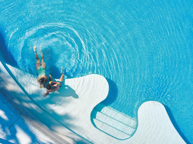 Persona che nuota in piscina blu chiaro con gradini arrotondati.