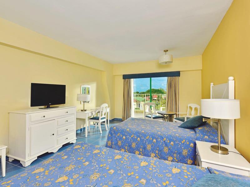 Camera d'hotel con due letti, TV, scrivania e accesso al balcone con vista.